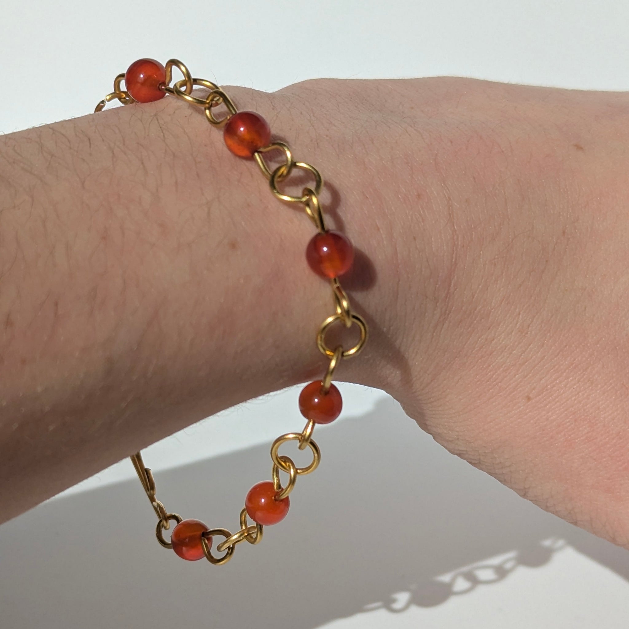 Gold bracelet with red beads on a wrist against a white background