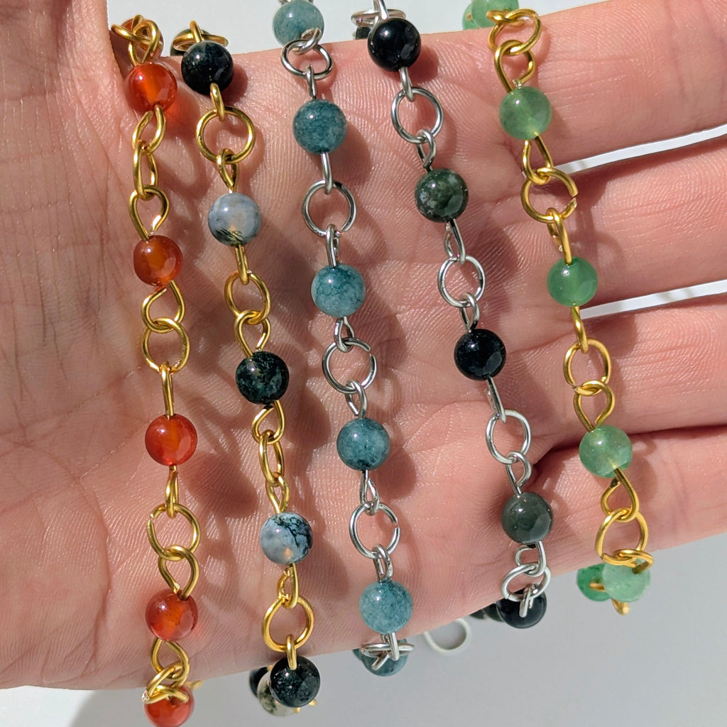 Three beaded necklaces with different colored beads on a hand against a white background