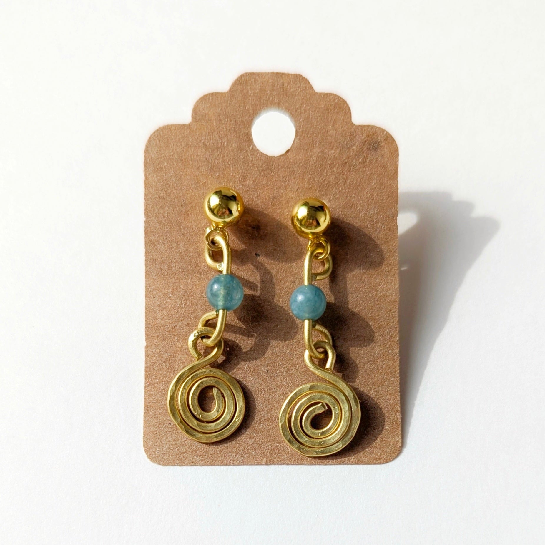 Gold spiral earrings with blue beads on a brown card against a white background