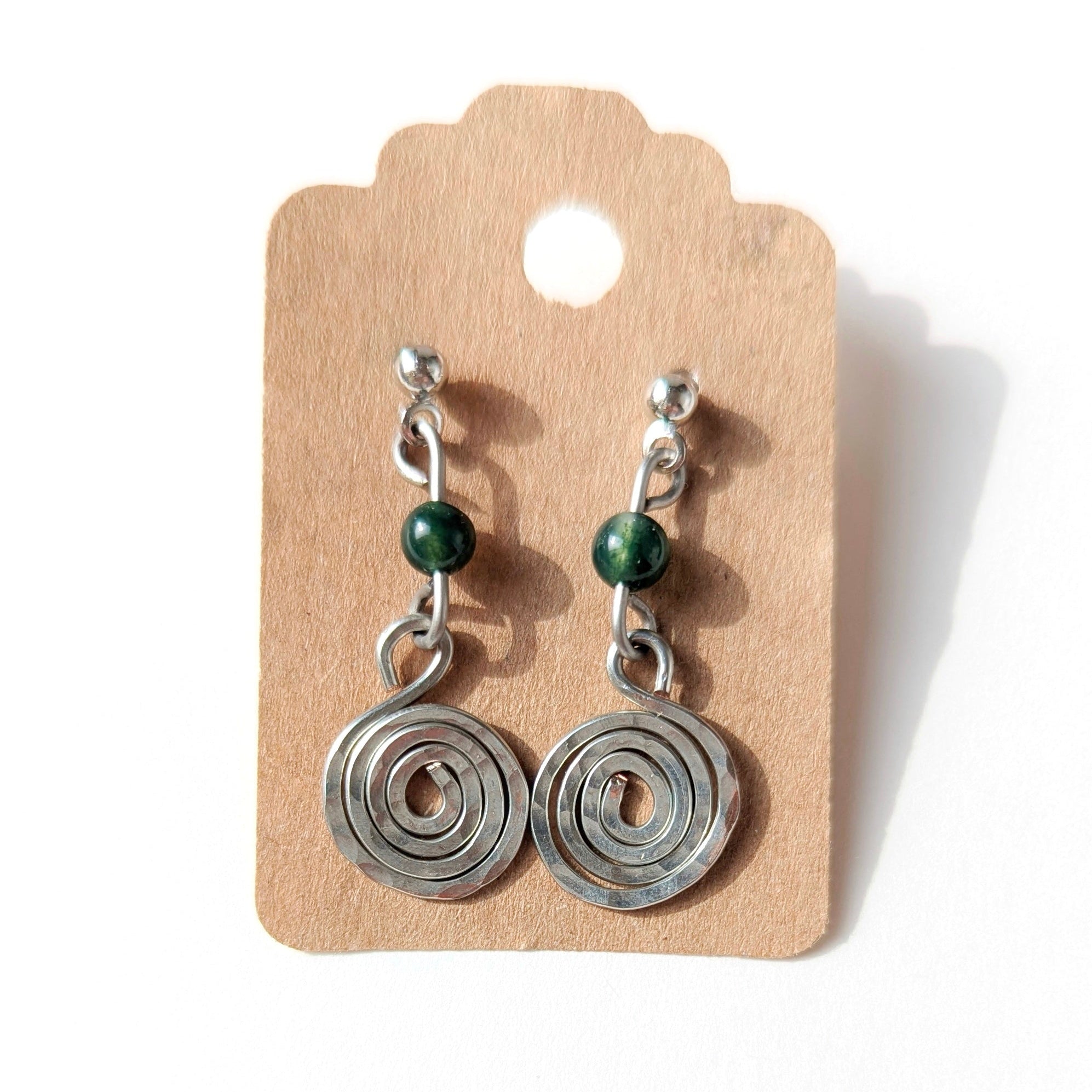 Pair of silver spiral earrings with green beads on a cardboard backing.