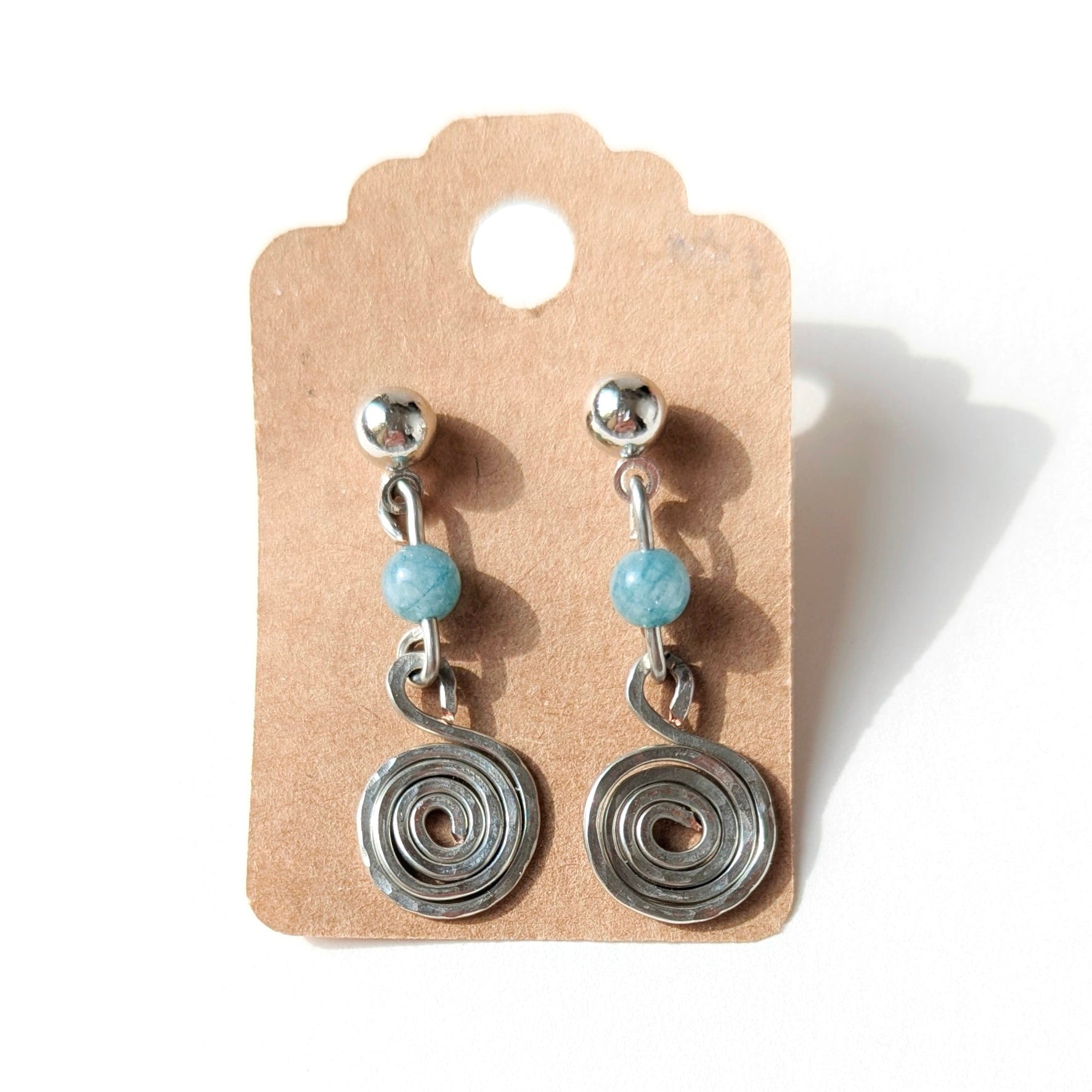 Pair of silver spiral earrings with turquoise beads on a cardboard backing.