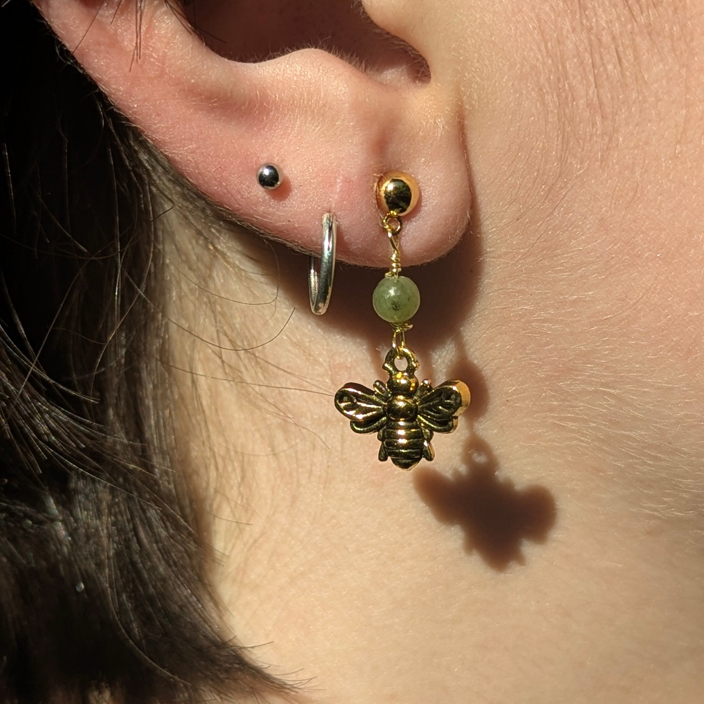 Close-up of an ear with a bee-shaped earring and a green bead.