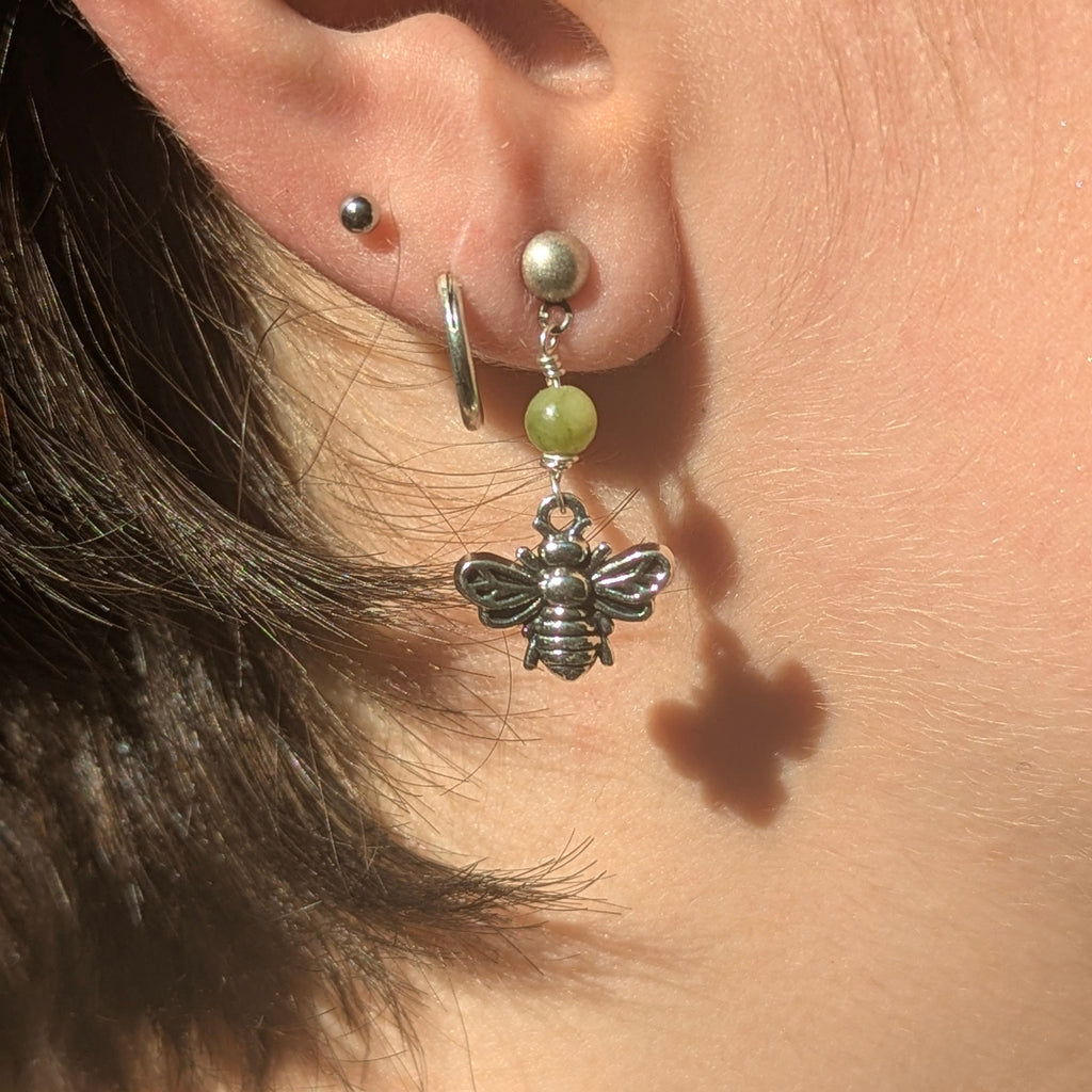 Close-up of an ear with a bee-shaped earring and a green bead.