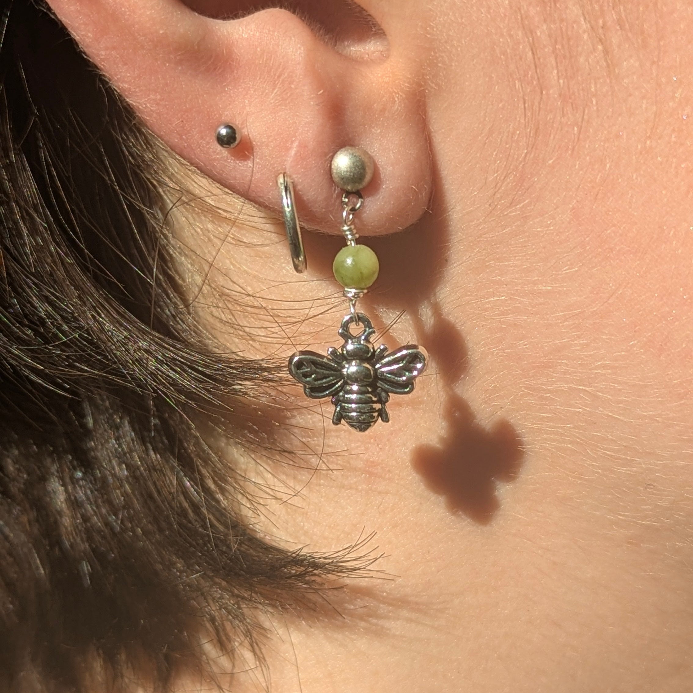 Close-up of an ear with a bee-shaped earring and a green bead.