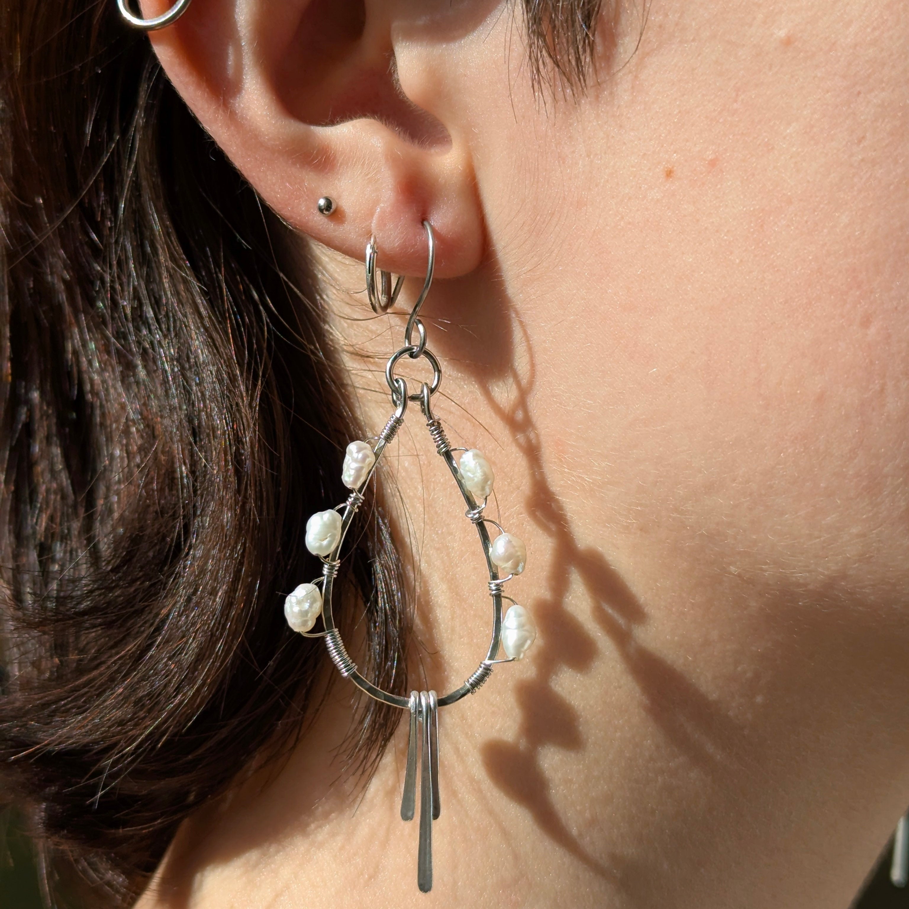 Close-up of a person wearing a silver earring with pearl-like beads.