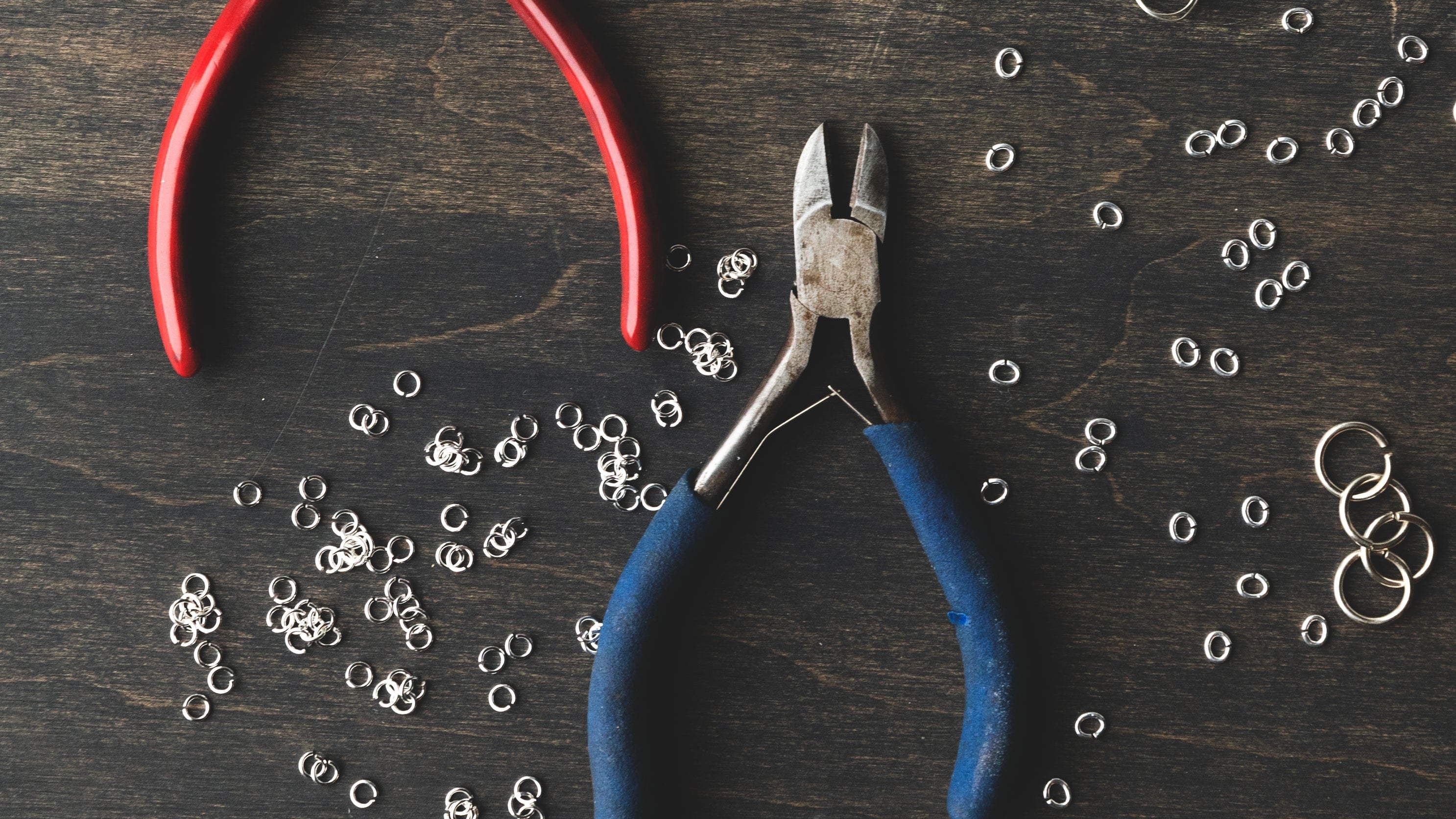Three pairs of pliers with red, blue, and silver handles on a dark wooden surface with small metal rings.