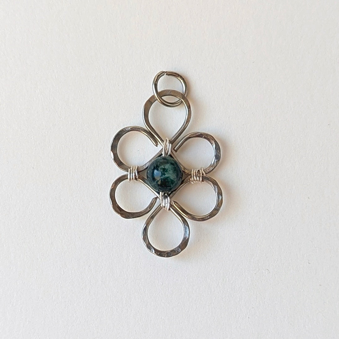 Silver floral pendant with a central gemstone on a light background