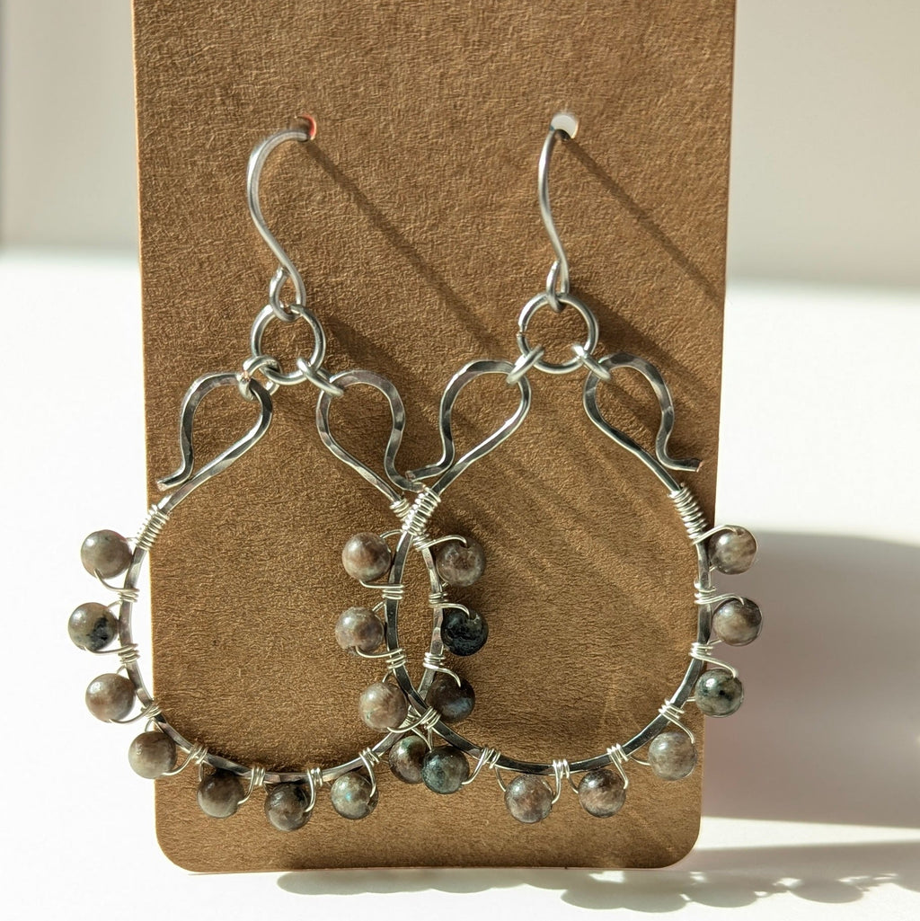 Silver hoop earrings with bead accents on a brown card against a white background