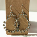 Silver hoop earrings with bead accents on a brown card against a white background