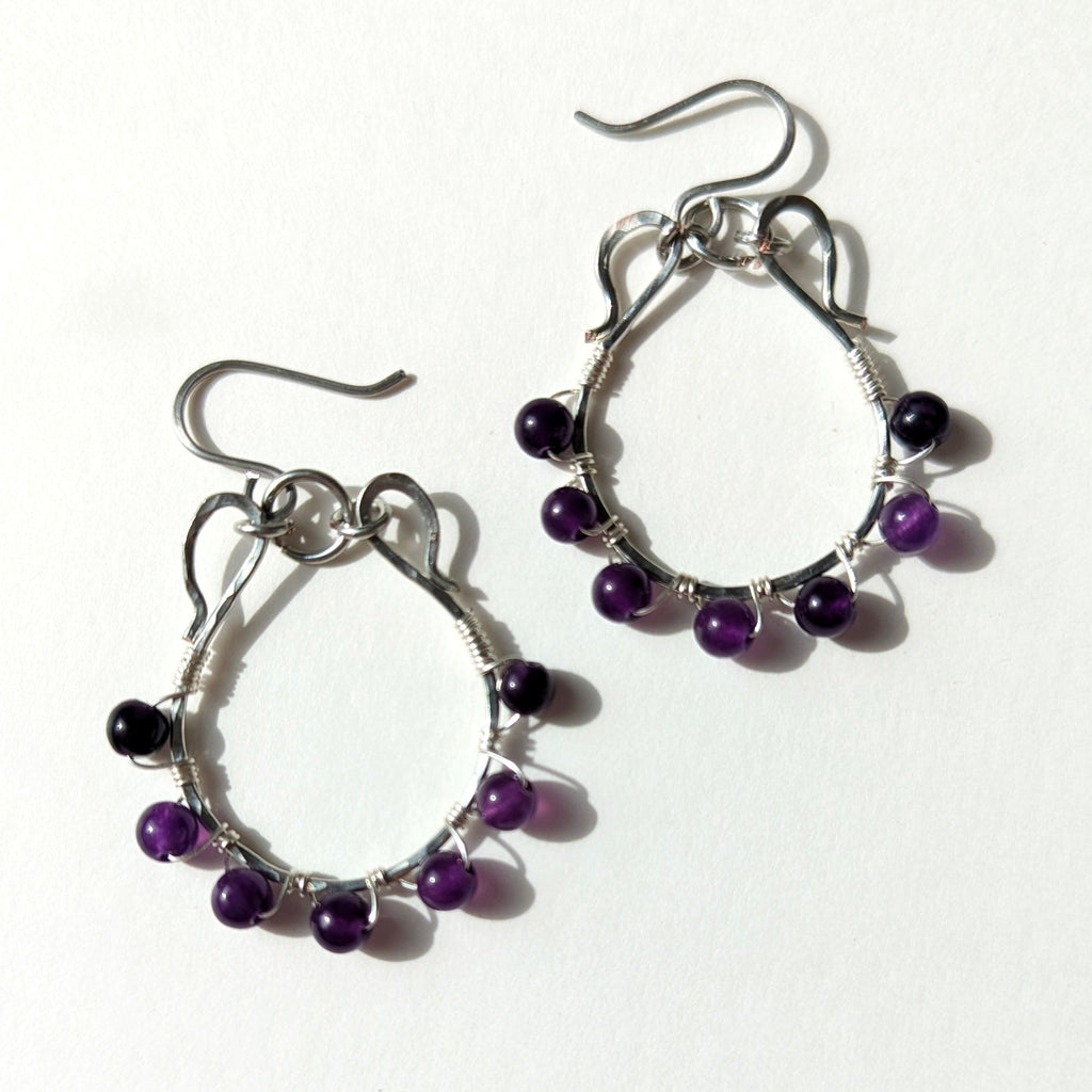 Silver hoop earrings with purple beads on a white background