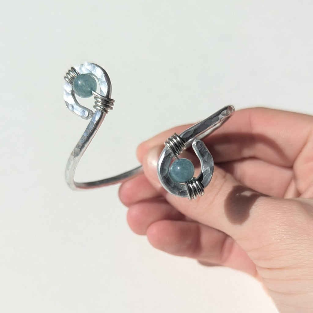 Hand holding a silver bracelet with turquoise stones against a white background